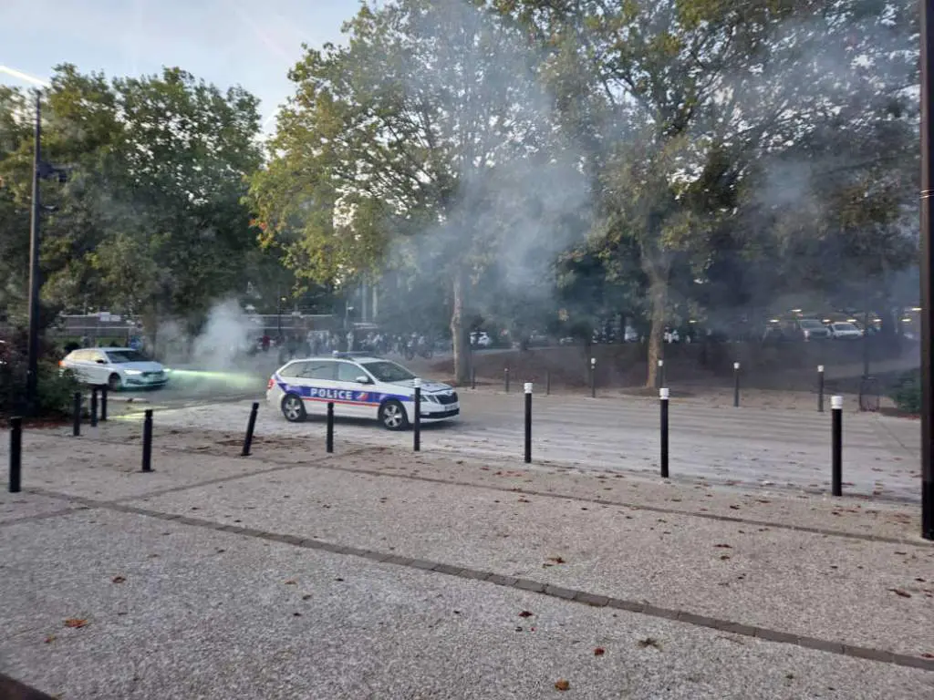 Une voiture de police devant le lycée Descartes. Du gaz flotte dans l'air. Au loin, un grand nombre de personnes vont visibles.