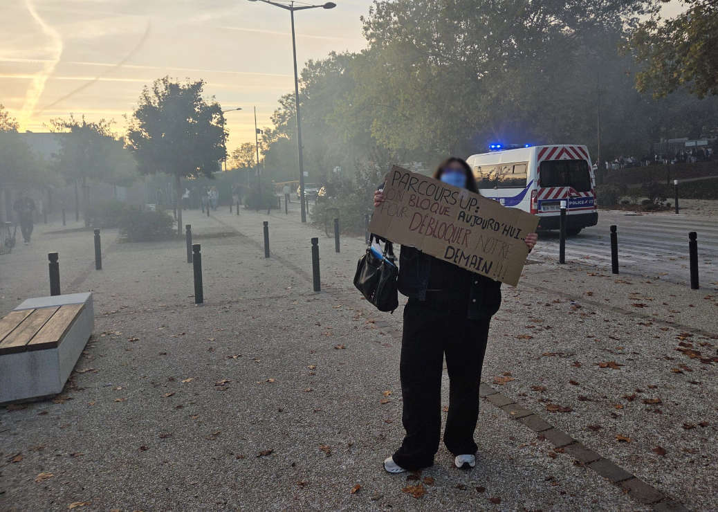Une jeune femme pose devant un car de police devant le lycée Descartes avec une pancarte "Parcoursup, on bloque aujourd'hui pour débloquer notre demain!